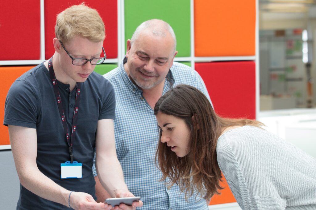 Two men and a women looking closely at a tablet screen