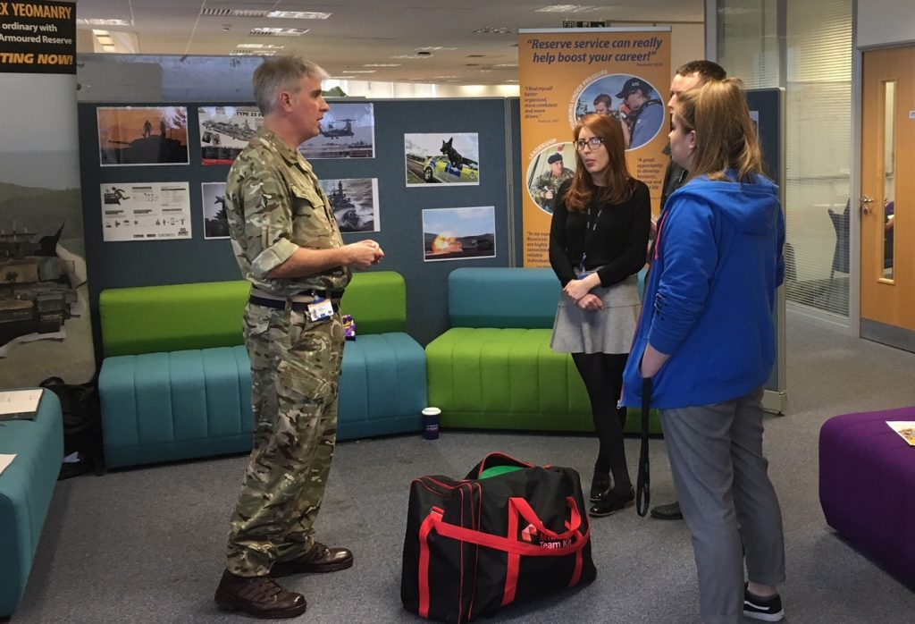 Civil Service reserve standing in front of his display stand talking to 3 members of staff