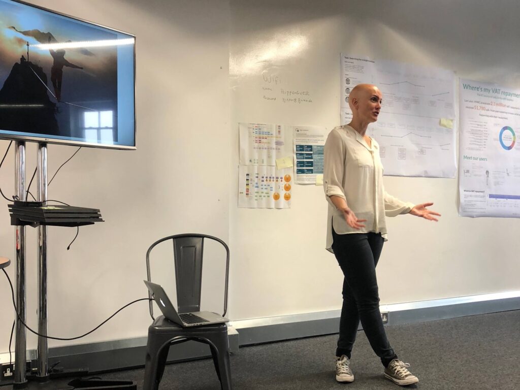 Alex Kean standing up in front of a presentation screen speaking to the audience