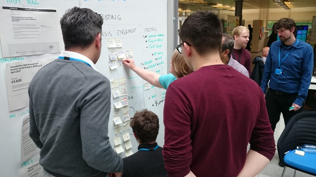 User researchers are gathered around a whiteboard discussing and putting up post it notes