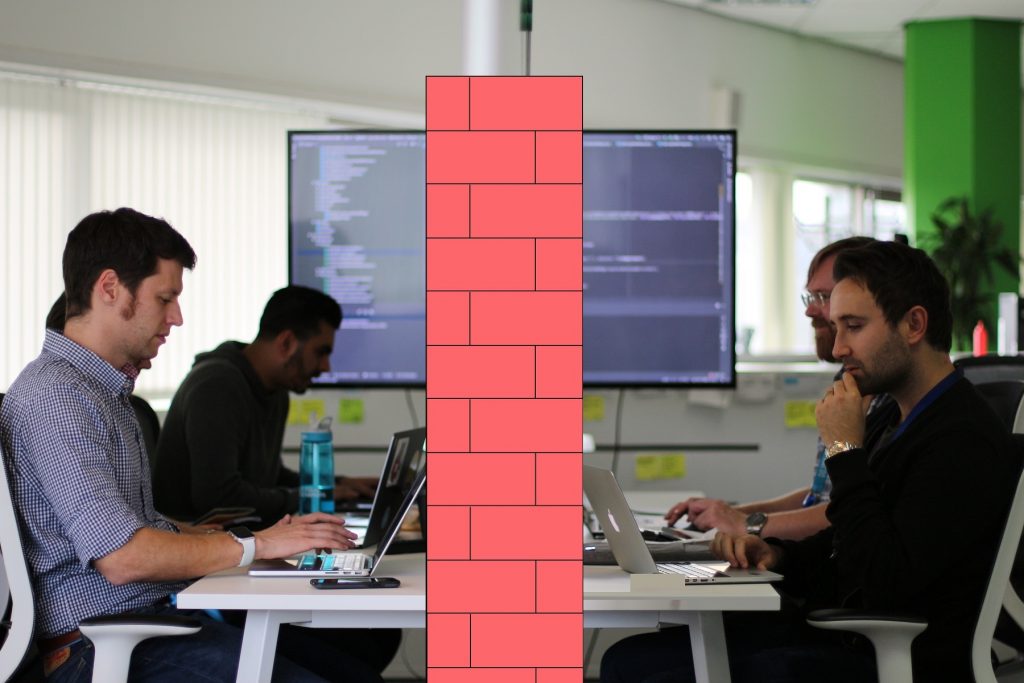 The dev ops team working on lap tops divided by a brick wall