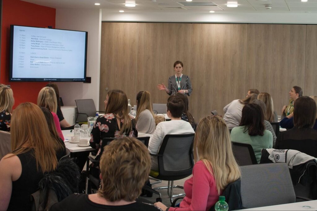 Chloe Walker presenting in front of a large screen and seated audience