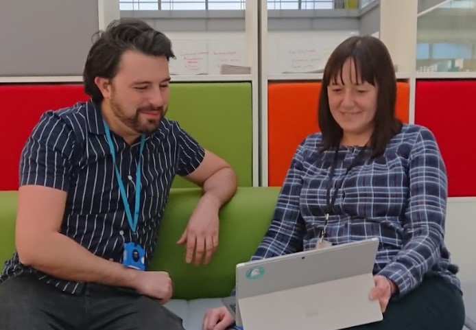 A male and female sitting on a colourful sofa looking at a laptop