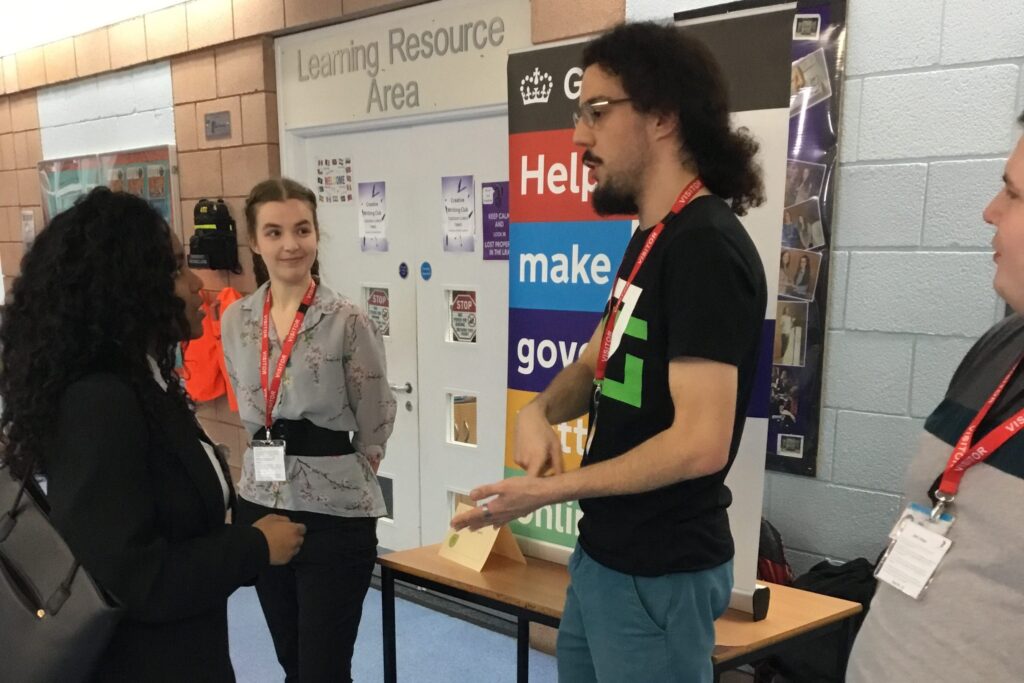 Louis Mannervy standing in front of the HMRC display talking to a female student