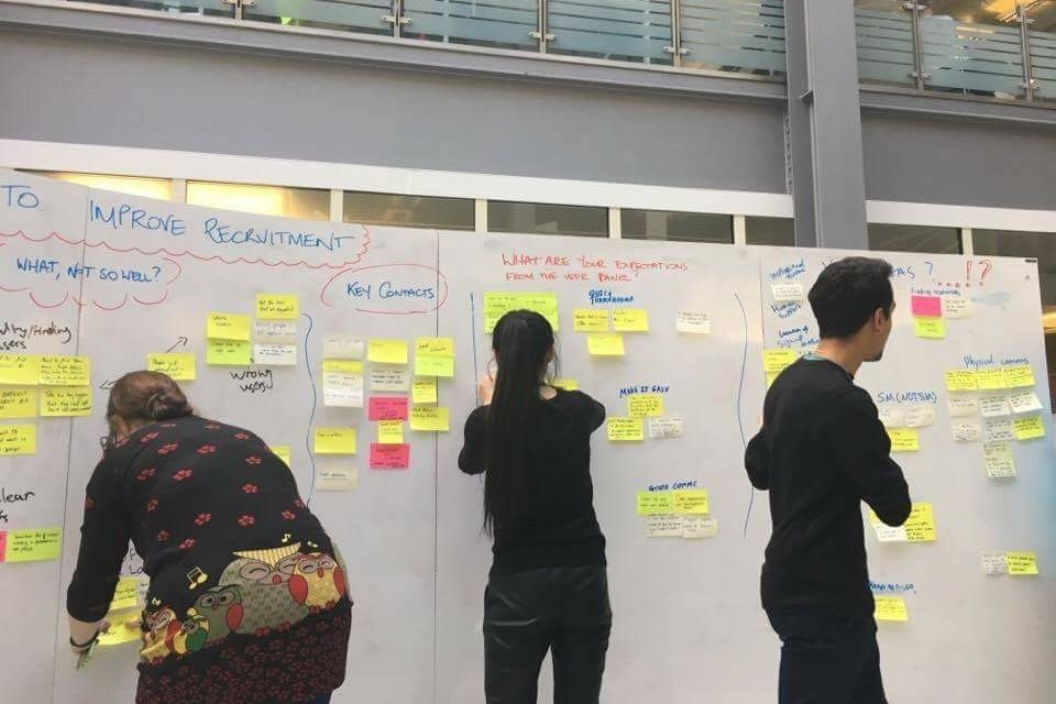 Three members of the User Research Services team standing at a whiteboard which is covered in colour sticky notes