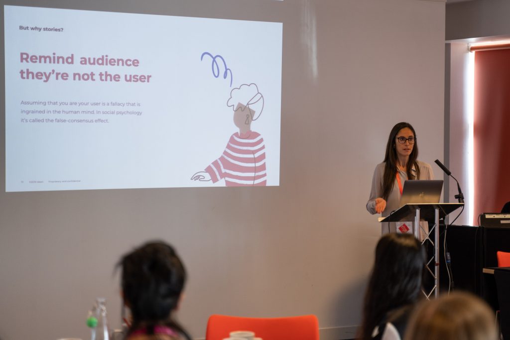 Image of a speaker standing in front of an audience with a large screen behind them