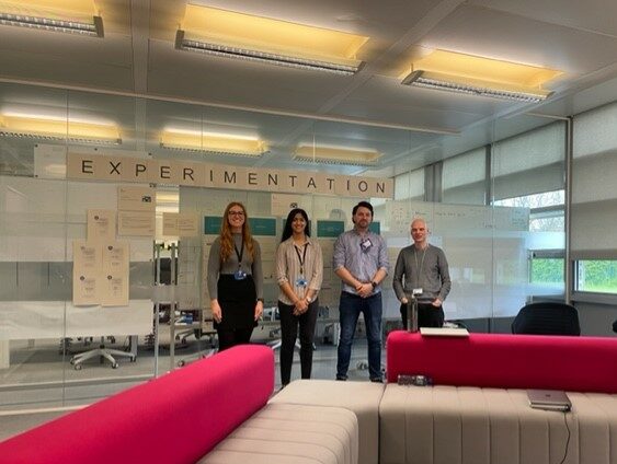 Four members of the HMRC experimentation team, smiling and standing in front of a whiteboard that they've been working on.