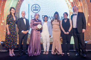 A group of HMRC employees standing on a stage at the Women in Tech Employer awards. They are holding a trophy and smiling for the camera